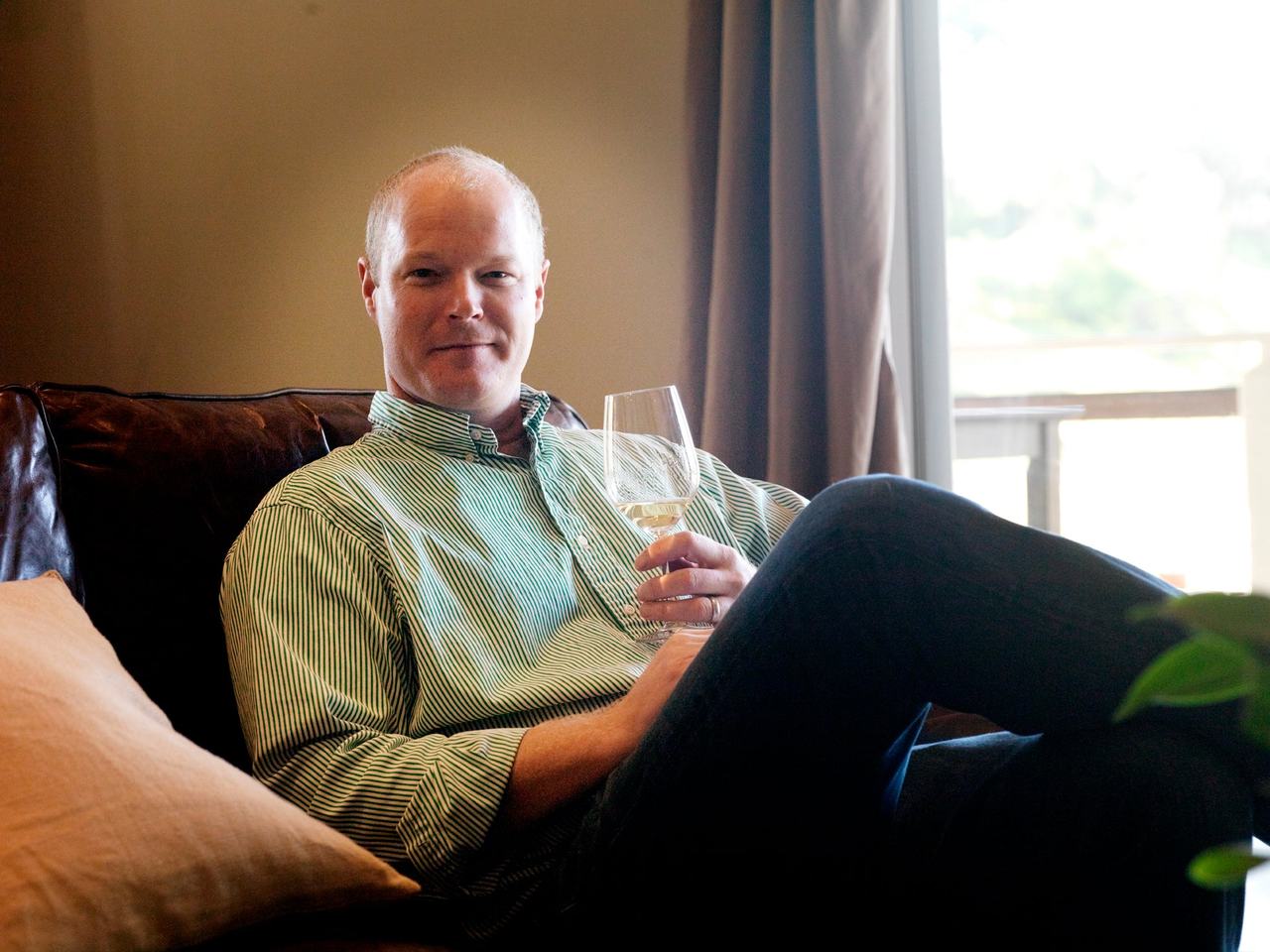 Kirk Venge seated on a leather sofa with a glass of white wine.