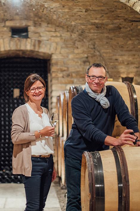 Vincent and Aline Bouzereau in the cellar, leaning on a barrel with glasses of white wine