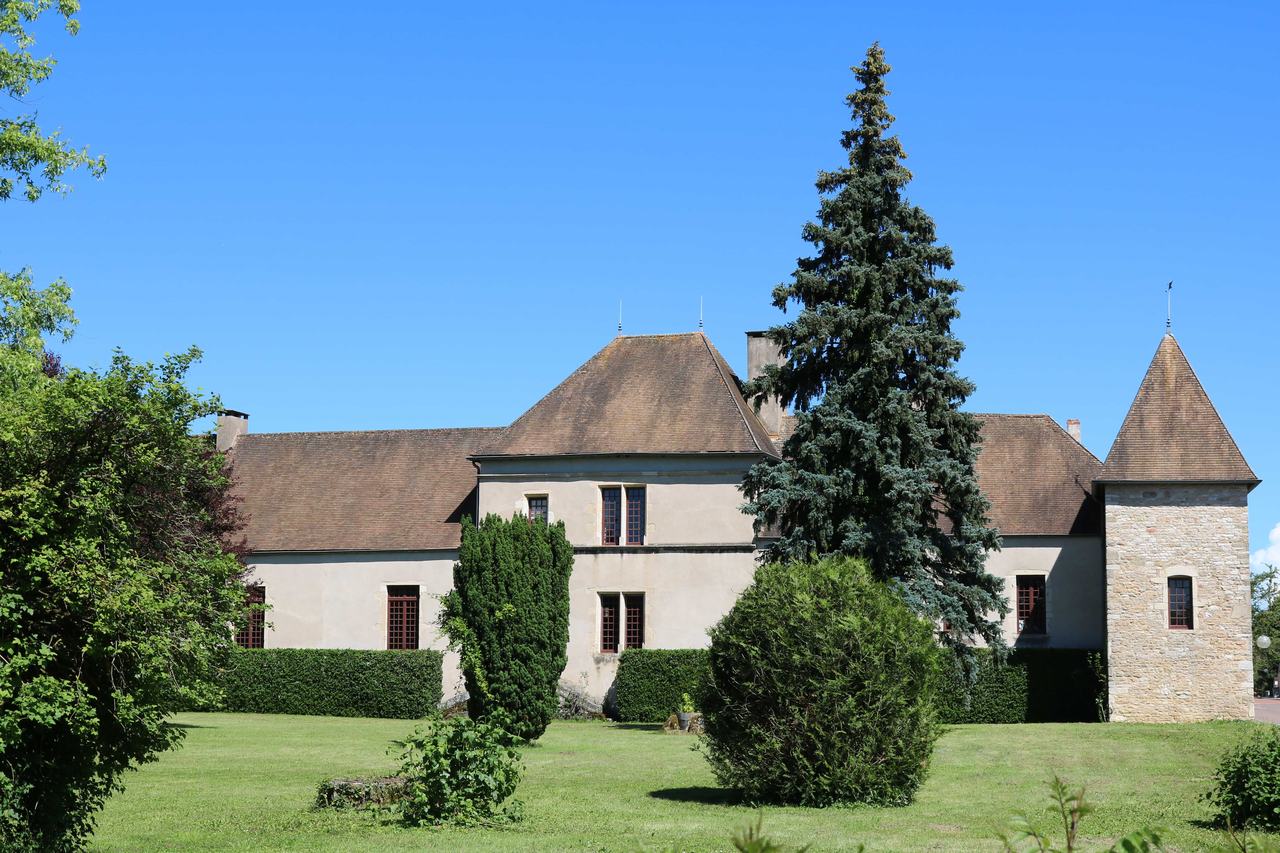 A long château with a stone corner tower and steep tiled roofs behind a lawn and a tall fir