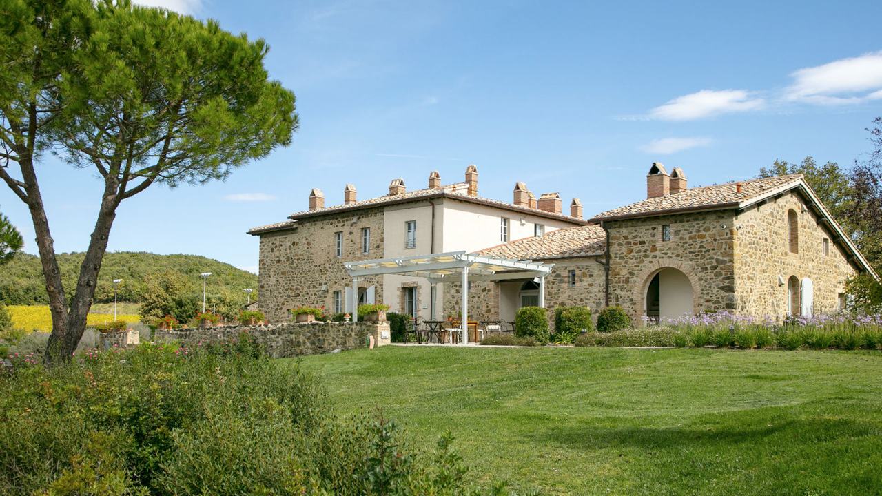 The stone farmhouse among umbrella pines and lawns.