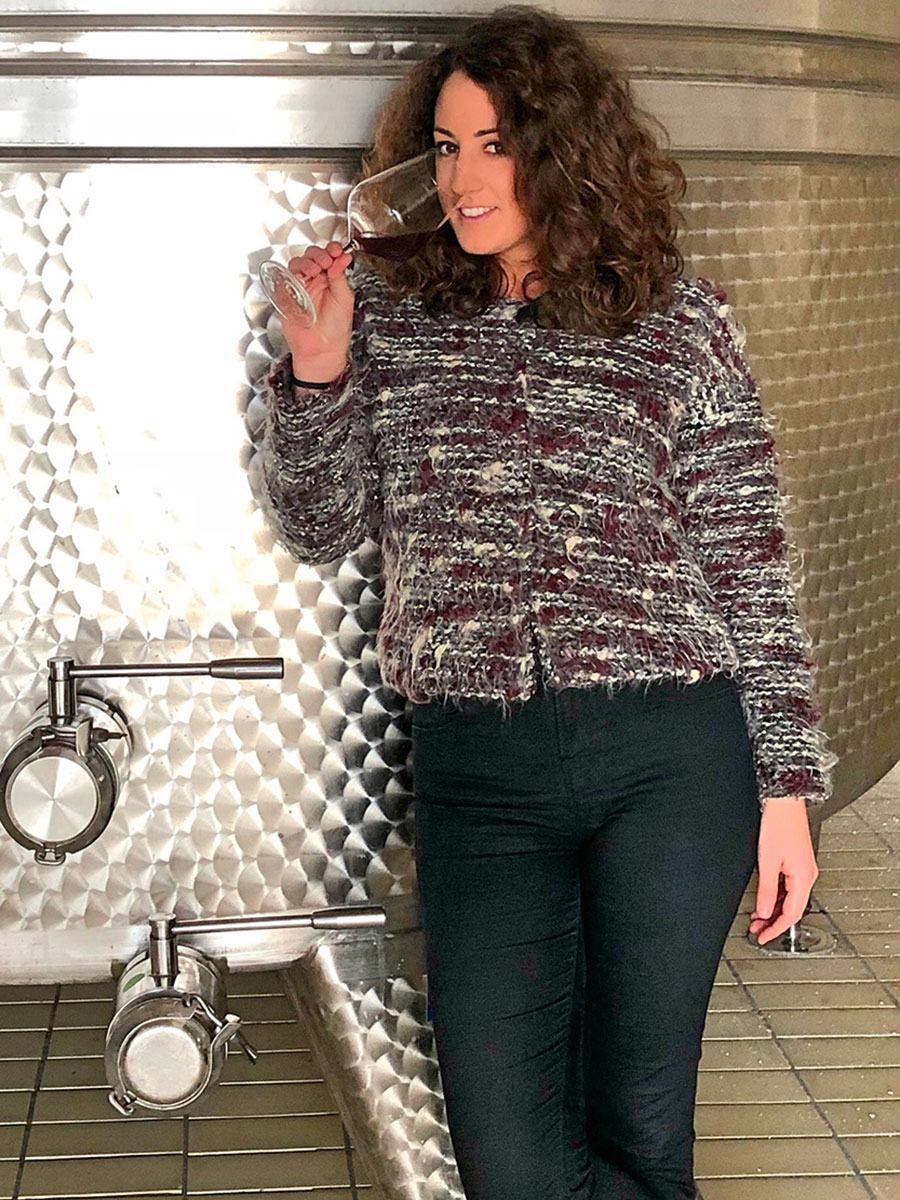 A woman tasting a glass of white wine against a steel tank in the cellar.
