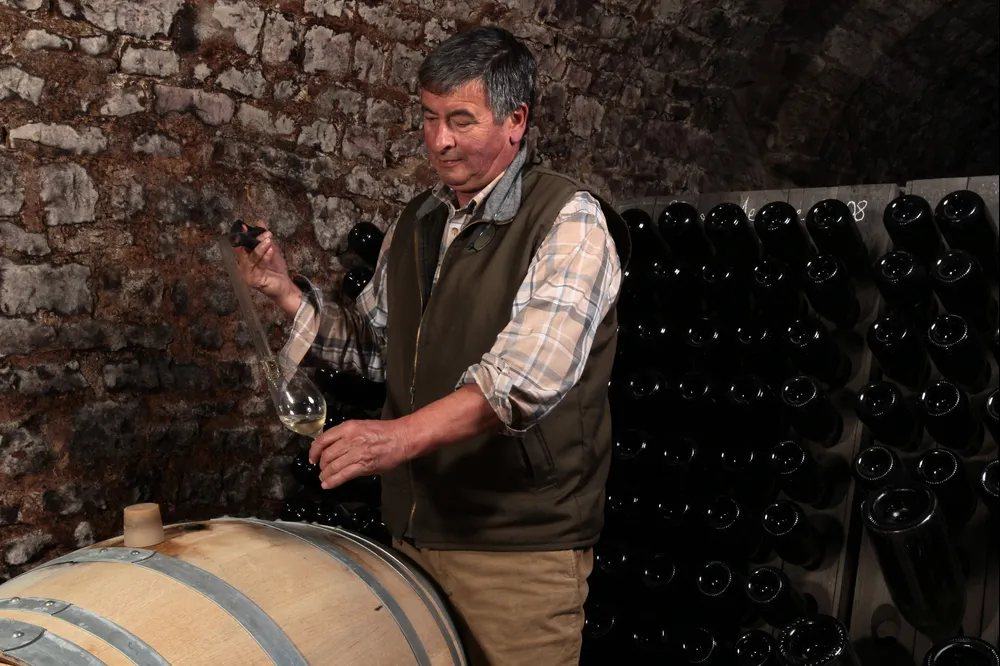 Richard Cheurlin drawing a sample from barrel in the cellar, bottles sur lattes behind