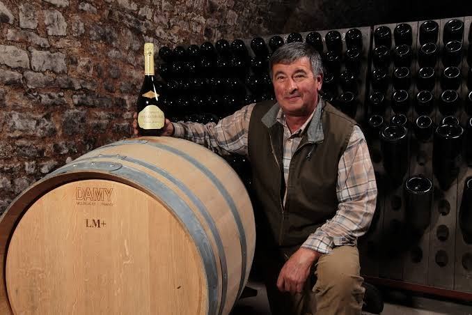 Richard Cheurlin seated on a barrel with a bottle, bottles sur lattes behind