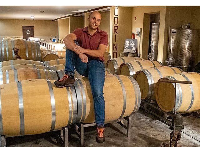 Stefano Corino sitting on a barrel in the cellar, the Corino name painted on the wall behind