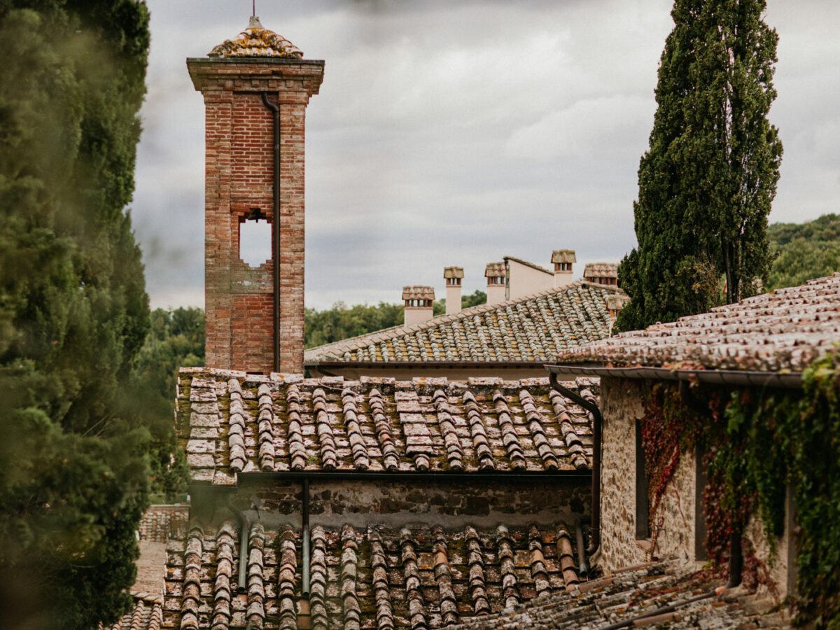 An old brick tower and tiled roofs of the estate buildings, with a cypress beside them.