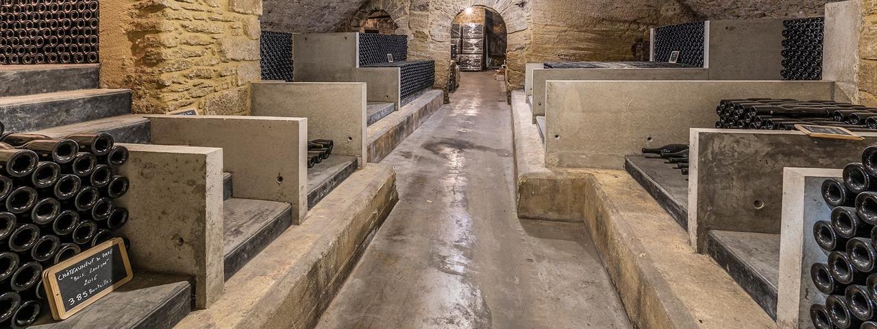 A vaulted stone cellar with concrete bins of bottles either side of an aisle