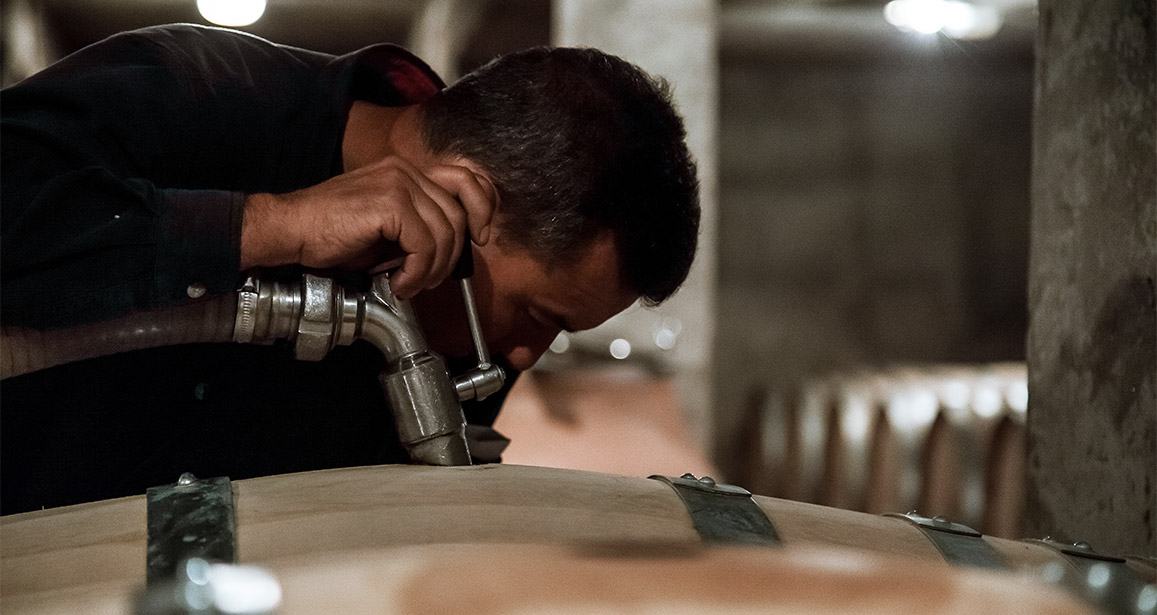 A man drawing a sample from a barrel in the cellar