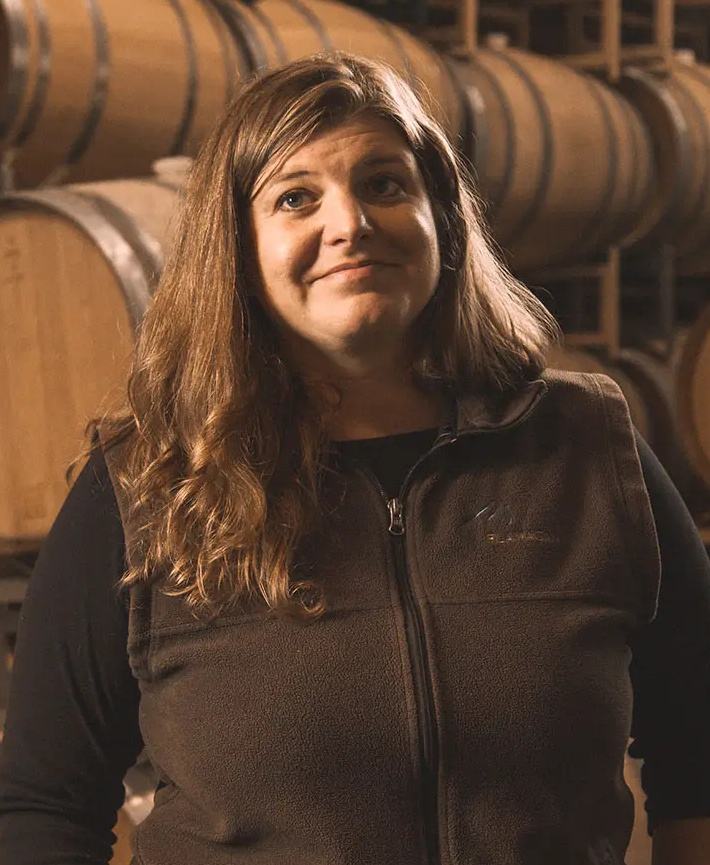 Winemaker Isabelle Mort in front of stacked barrels.
