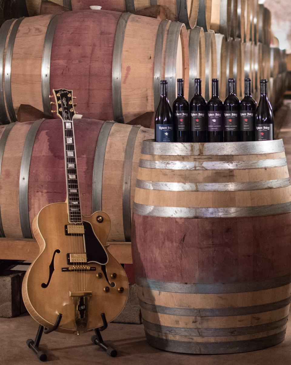 An archtop guitar on a stand beside stacked barrels in the cave