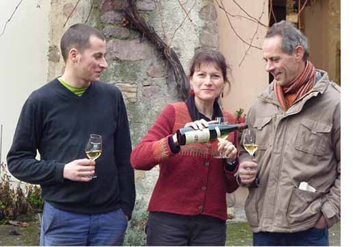 Two men and a woman taste white wine in the courtyard of the domaine.