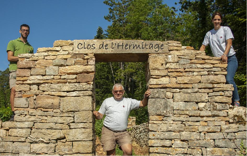 Three people at a dry-stone wall gateway marked Clos de l'Hermitage