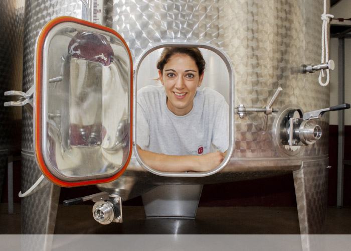 A young woman smiling through the open hatch of a stainless steel tank