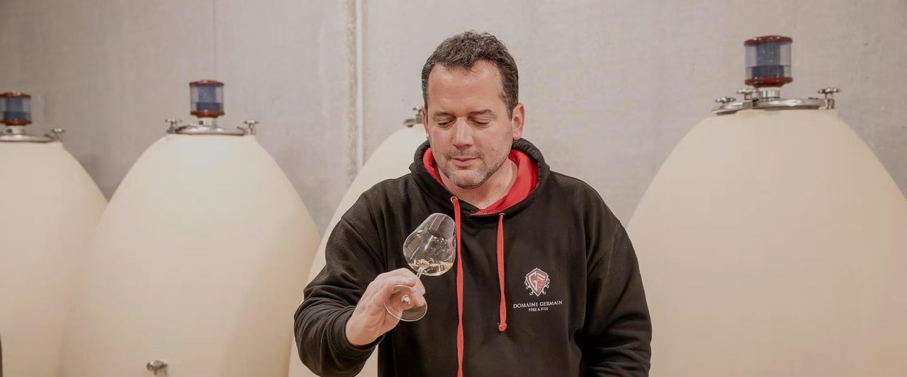 Arnaud Germain tasting a glass of white wine between concrete egg vats.