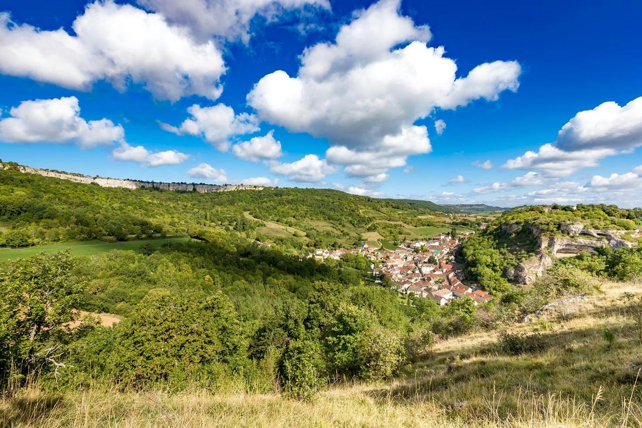 Green slopes and limestone cliffs above the valley at Saint-Romain under a blue sky.