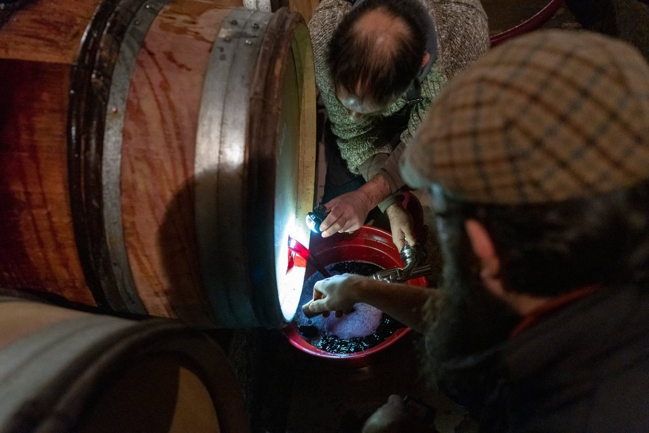 Two men drawing wine from a barrel by torchlight in the cellar.