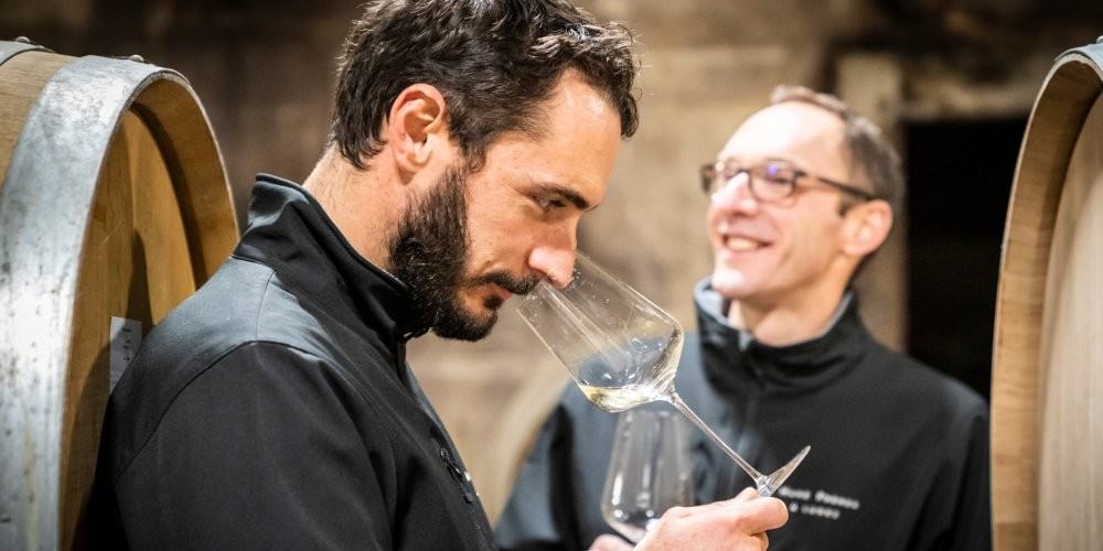 François Huré nosing a glass beside the barrels, his brother Pierre smiling behind him