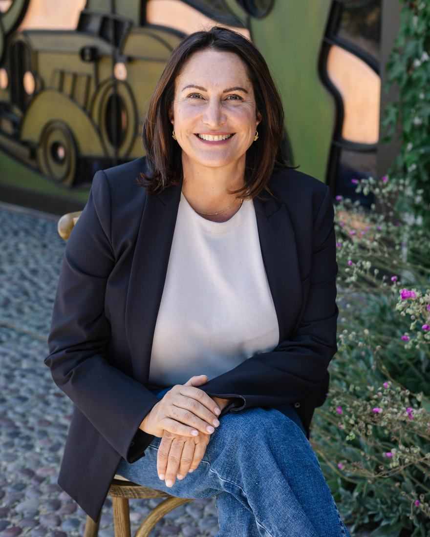 Ana Keller seated outdoors in front of a stained-glass panel, smiling.