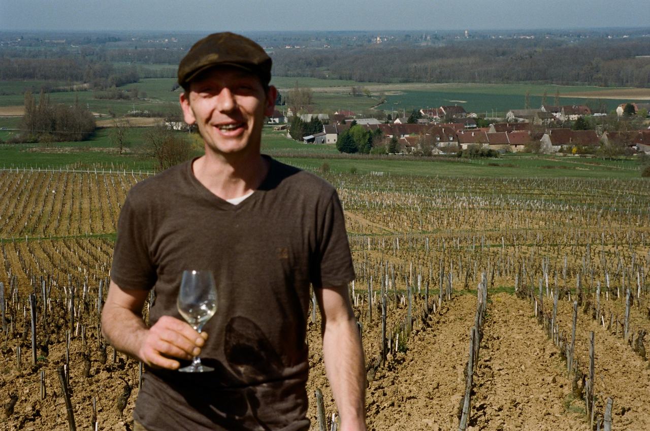 Julien Labet with a glass among the bare winter vines above Rotalier, the village and the plain behind.