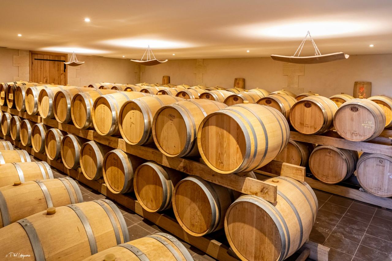 Rows of oak barrels stacked two high in a lit stone cellar