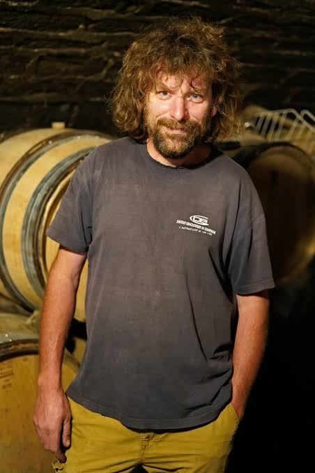 Laurent Pataille in a grey T-shirt in the cellar, barrels behind him.