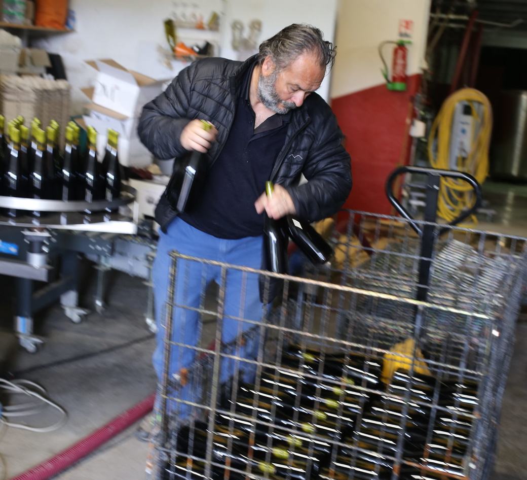 A man loading freshly filled bottles into a wire cage.