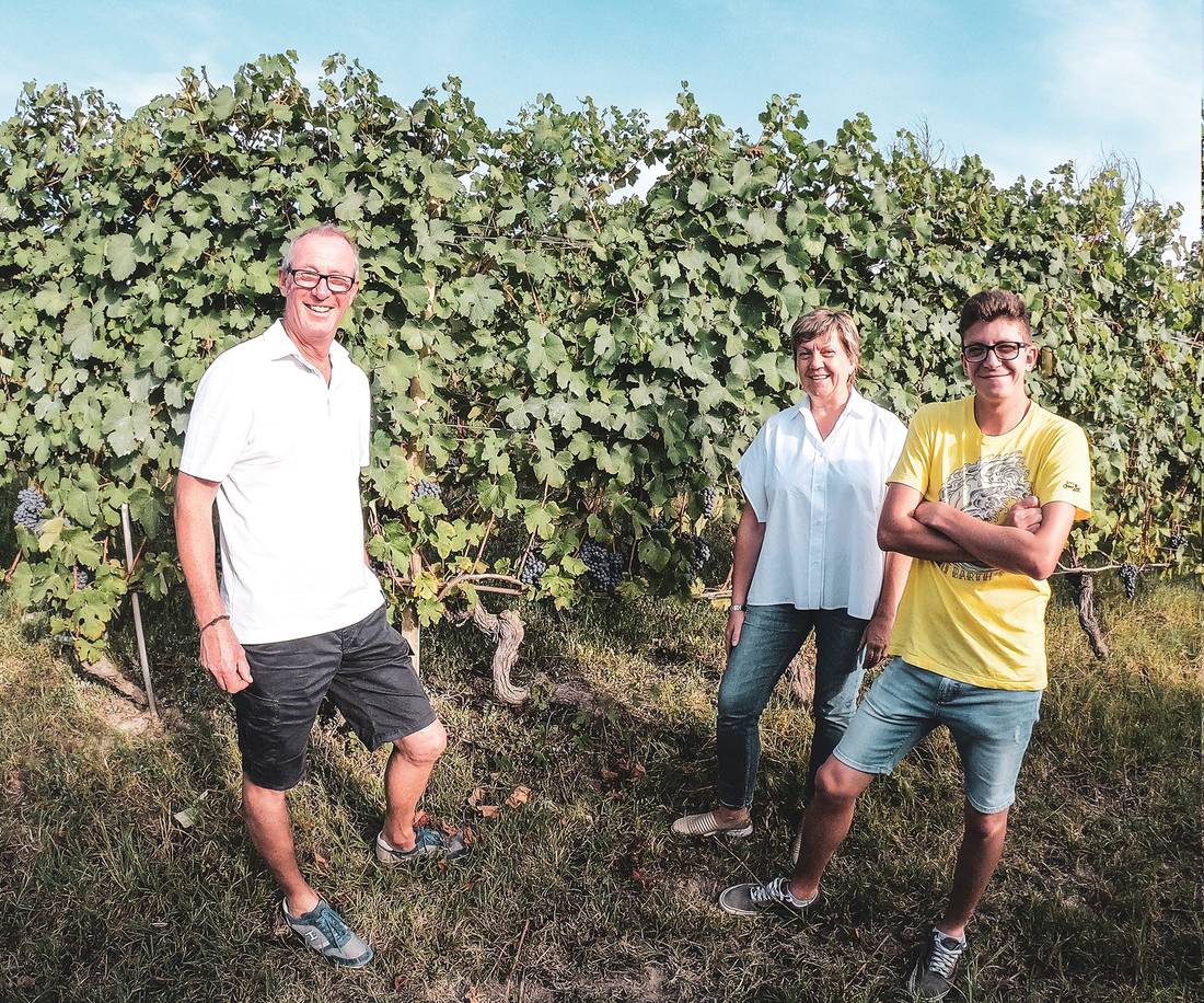 Two men and a woman standing in front of a wall of vines in summer.