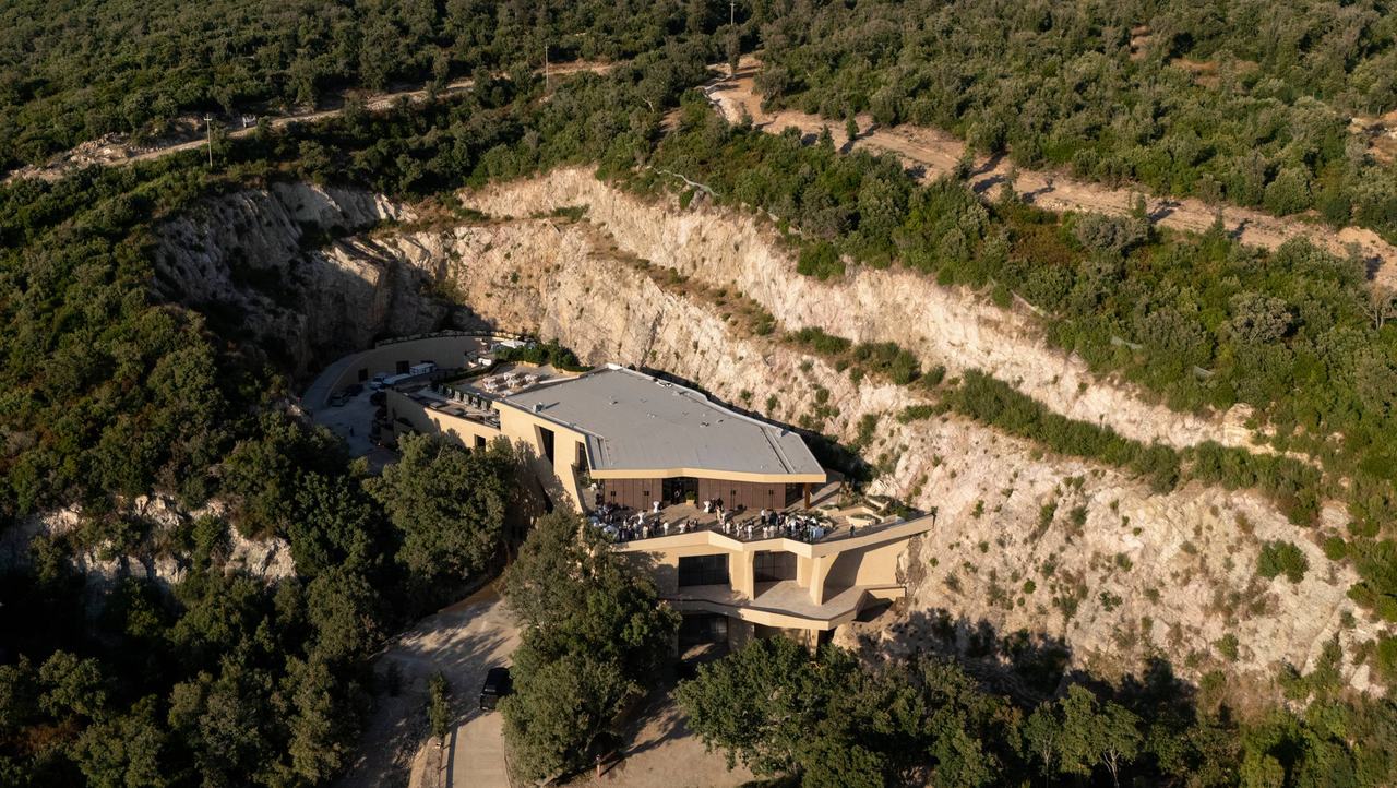 Aerial view of the Meraviglia winery built against a pale rock face, surrounded by woods.