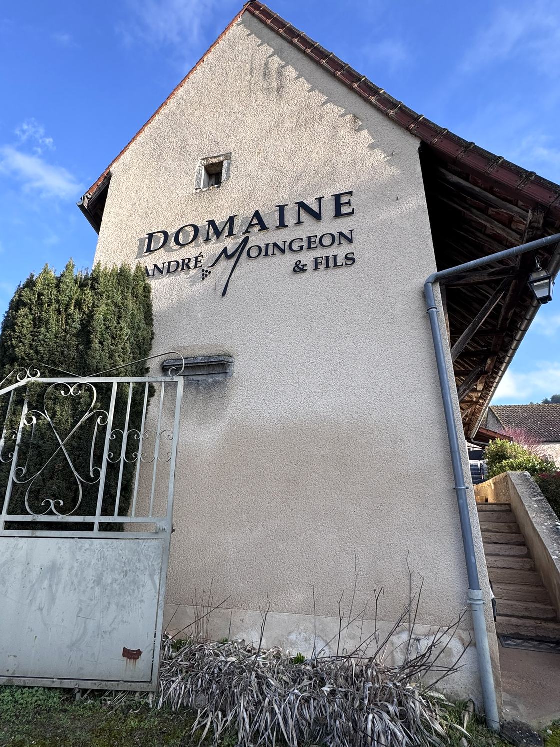 The gable end of the winery with Domaine André Moingeon & Fils lettered on the wall, iron gate in front.