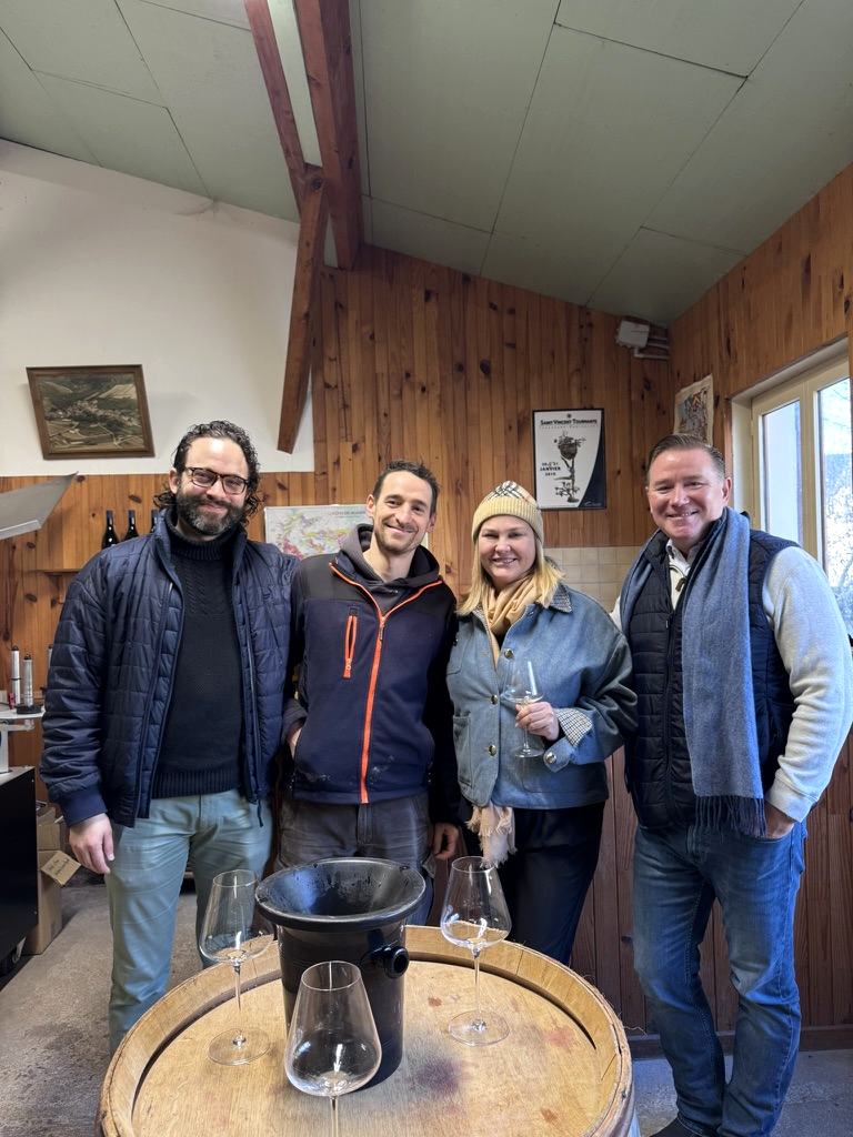 Four people with glasses around a barrel in the tasting room at Domaine Moingeon, Saint-Aubin.