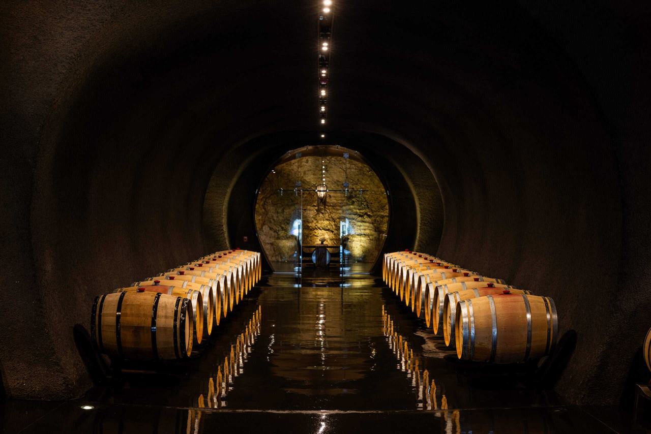 Two rows of barrels along a long lit cave tunnel