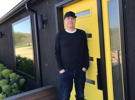 Juan Mercado in a cap and black sweater at the yellow door of the winery.