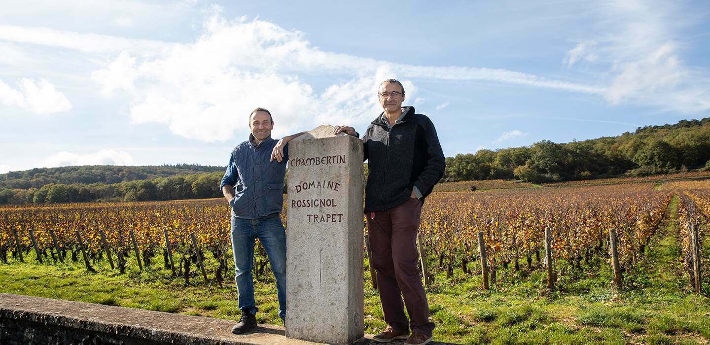 David and Nicolas Rossignol either side of the Chambertin stone marker, the vines gold behind them in autumn