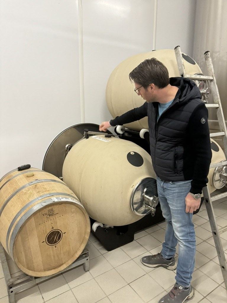 Alexandre Salmon in the cellar at Chaumuzy, a hand on one of the ceramic jars, a Vicard barrel beside him