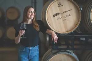Cleo Pahlmeyer with a glass of red wine, leaning on a Wayfarer barrel