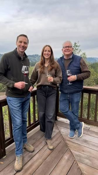Todd Kohn, Cleo Pahlmeyer and Joe Hunter with glasses of Pinot Noir on a wooden deck above wooded hills
